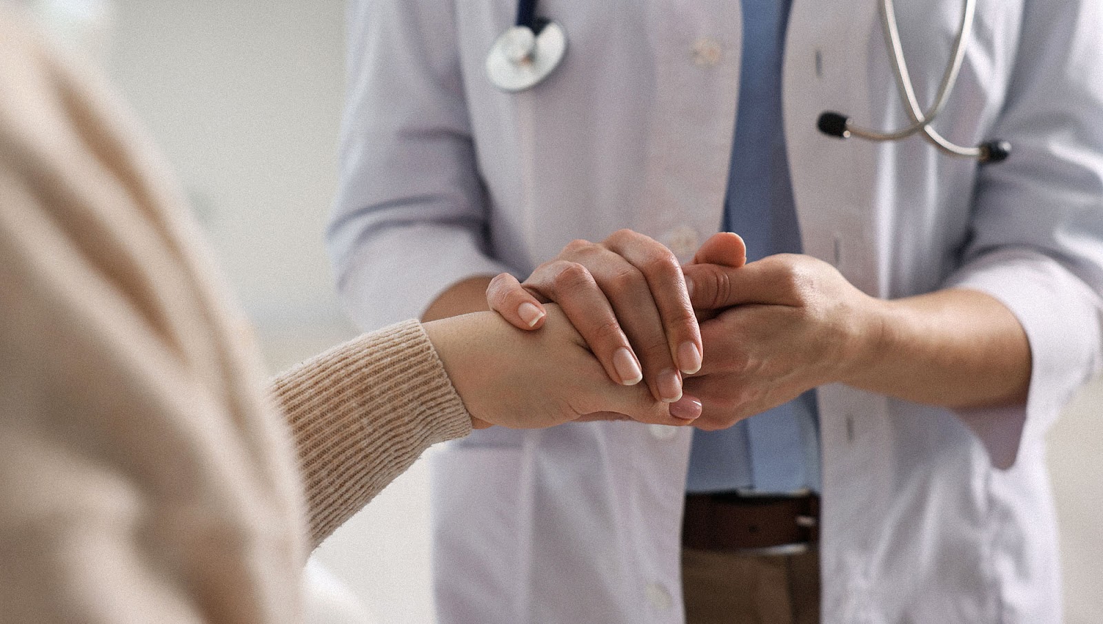 A healthcare professional holding the hand of a female patient to express support. 