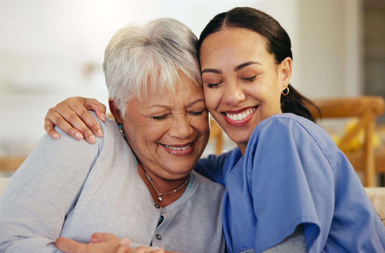 A caregiver hugging a smiling older adult with memory loss on the couch in memory care.