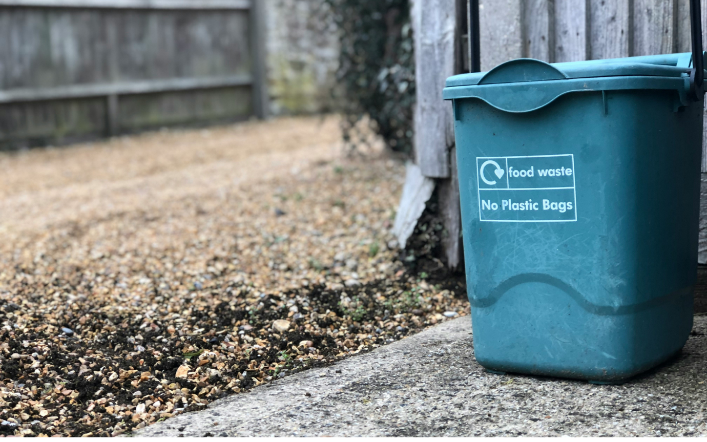 A blue trash can next to a fenceDescription automatically generated