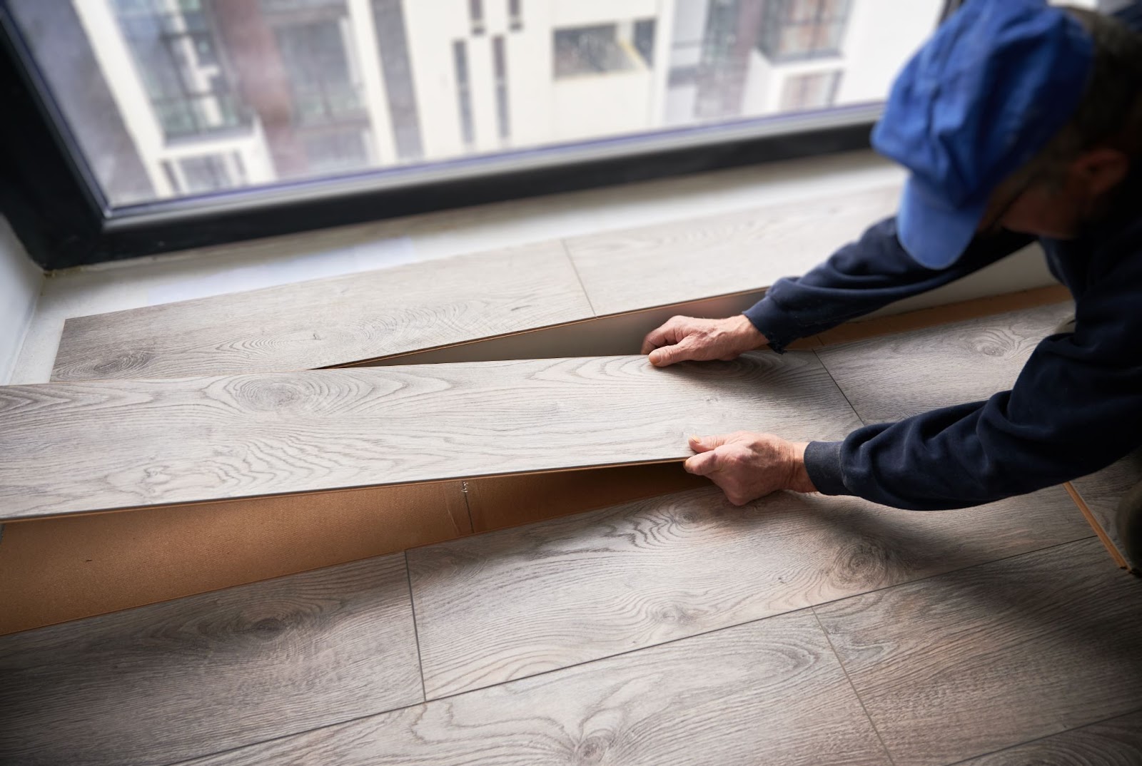  A construction worker in working clothes lays laminate flooring in an apartment under renovation.