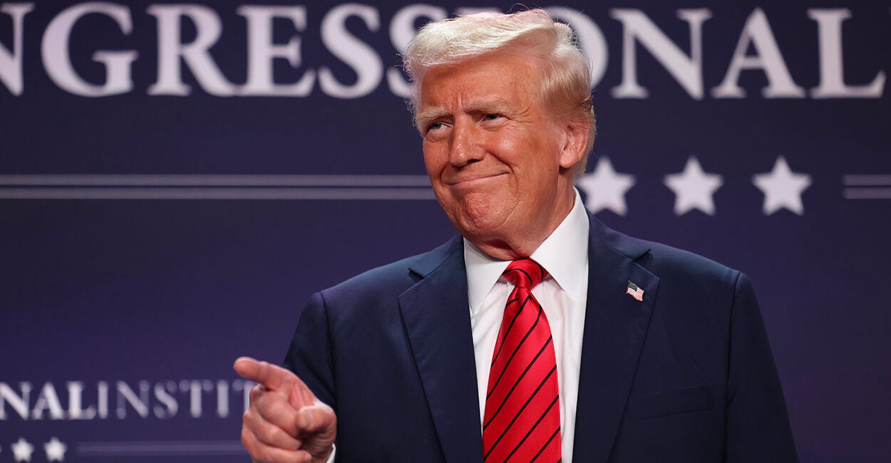 President Donald Trump points and smiles while wearing a blue suit with a red tie