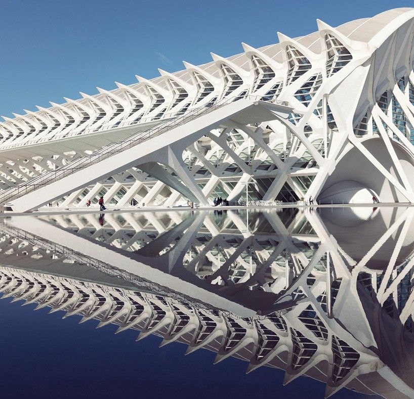 Captured by talented photographers, a modern architectural structure with sharp geometric lines and white surfaces is reflected in a calm body of water, creating a symmetrical mirror image.