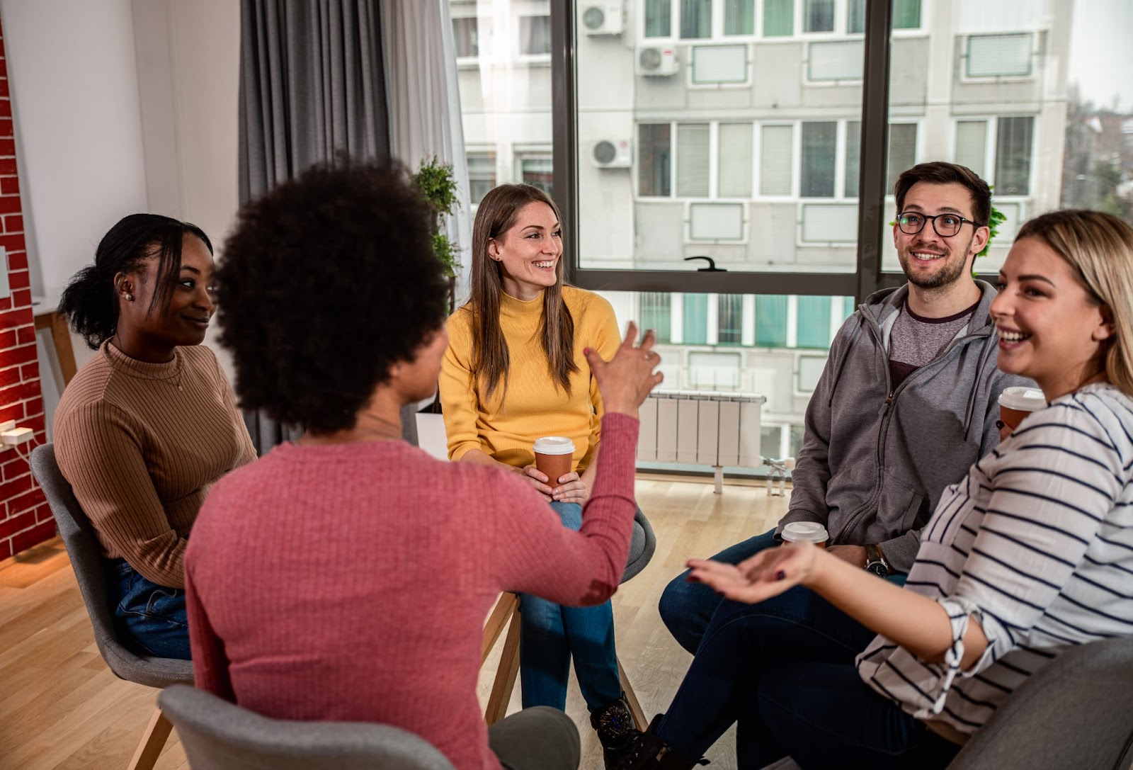 Group of people sitting in a circle and holding cups of coffee. 