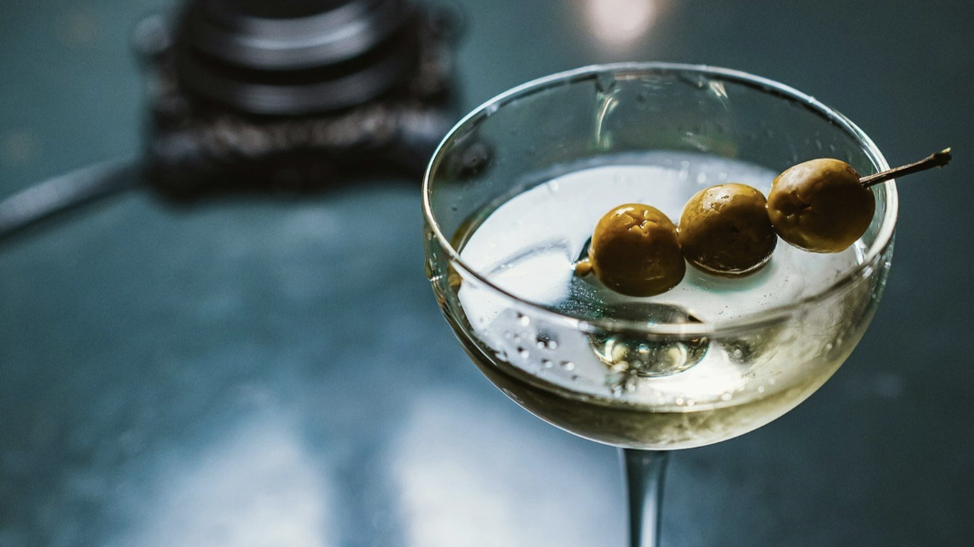 A coupe glass has a martini cocktail with three green olives