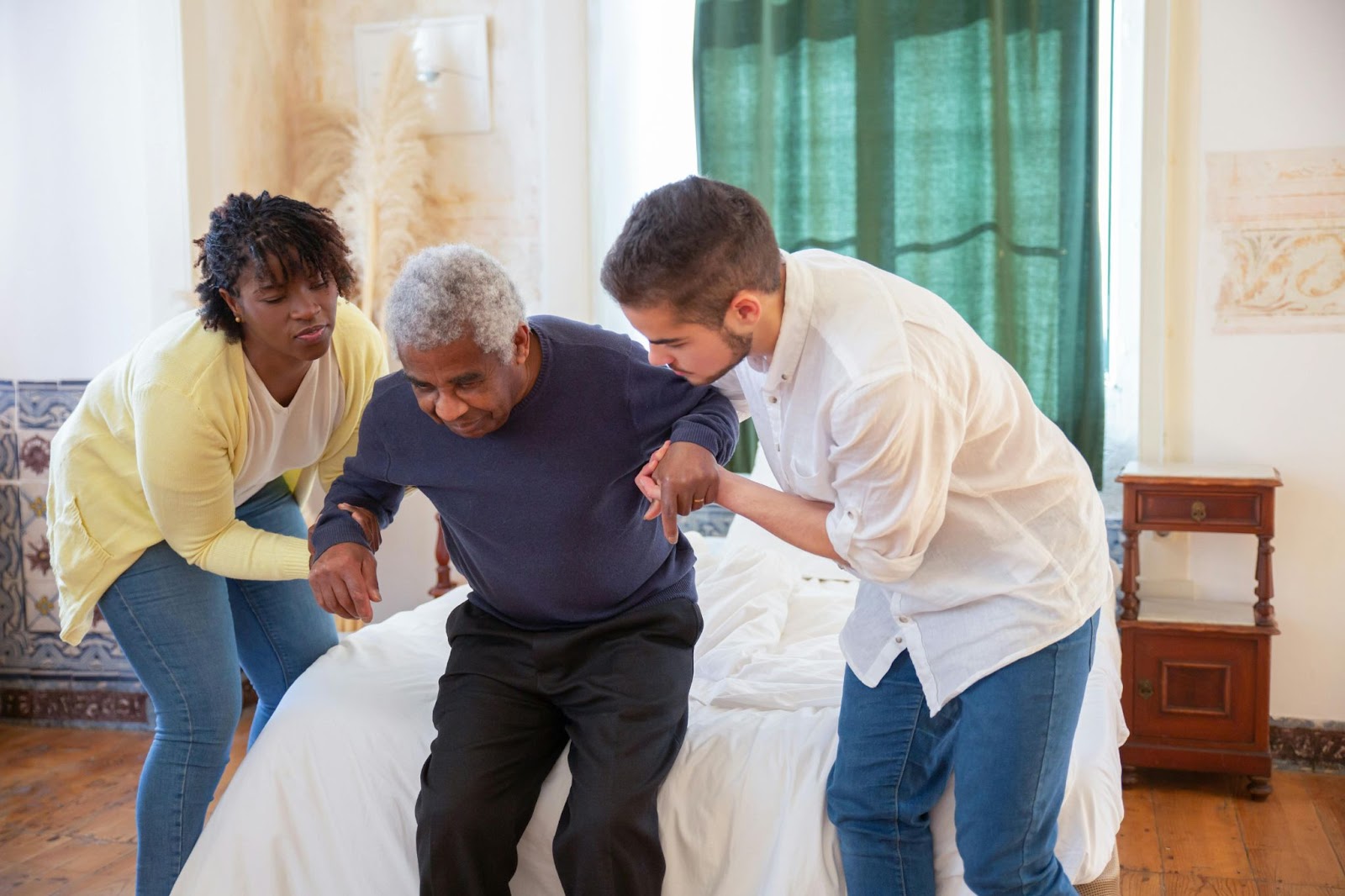 An older adult receiving dementia care services in his home and being lifted out of his bed by two caregivers