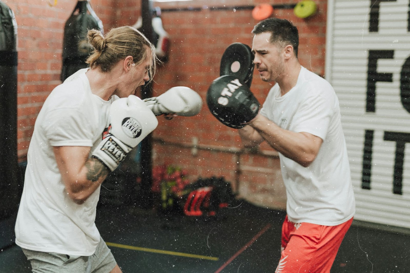 Two practitioners sparring in boxing, wearing gloves and headgear. One throws a punch while the other moves to defend