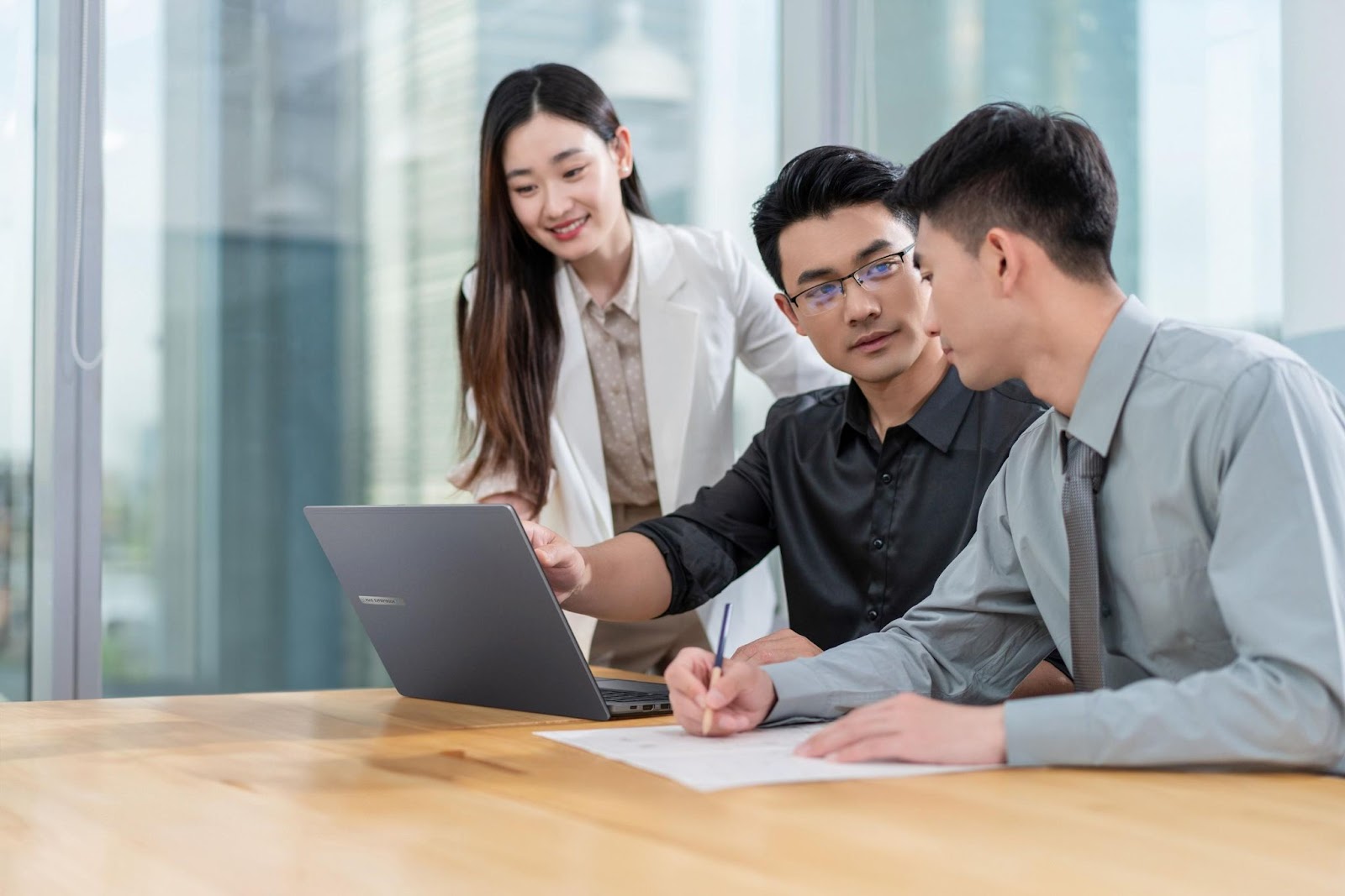 Três pessoas no escritório com um notebook corporativo em uma reunião.