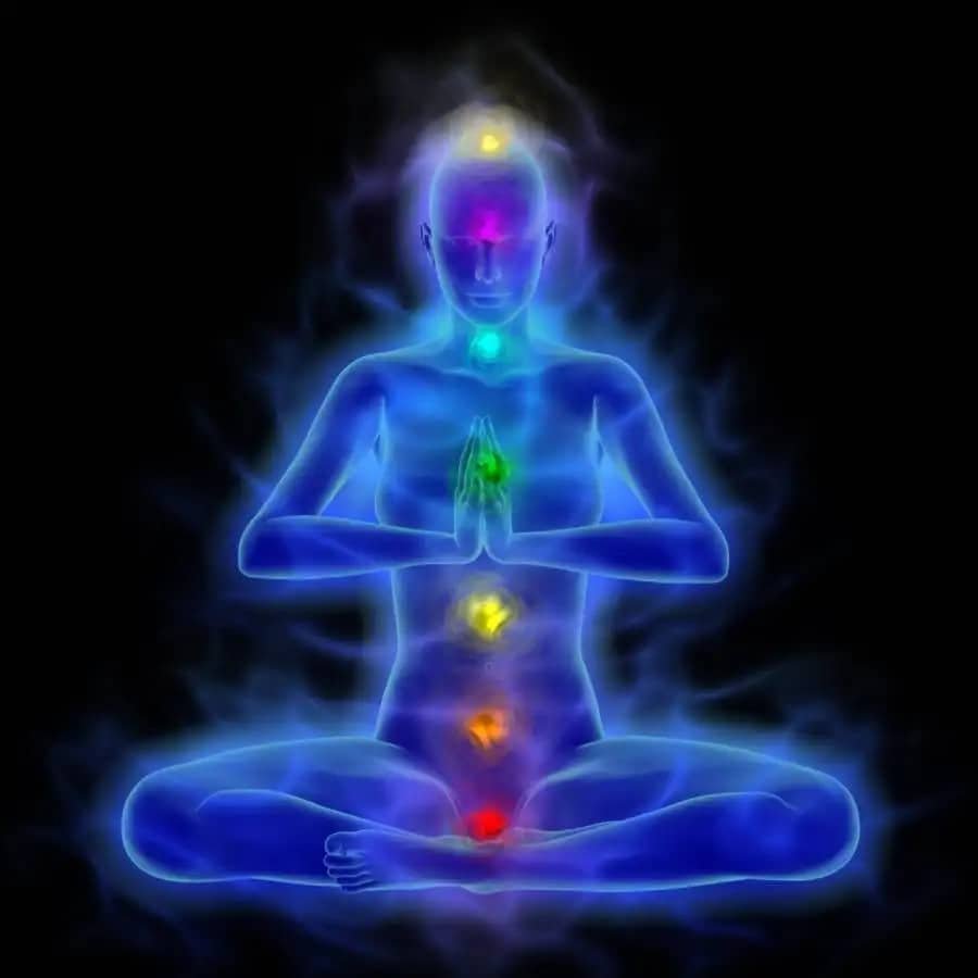 A representation of a human figure in a meditative pose with seven distinct colored areas aligned along the center of the body, often associated with chakras. These colored areas range from red at the base of the torso to violet at the top of the head, correlating to different chakra points. The figure is surrounded by a soft glow, enhancing the mystical or spiritual aesthetic.