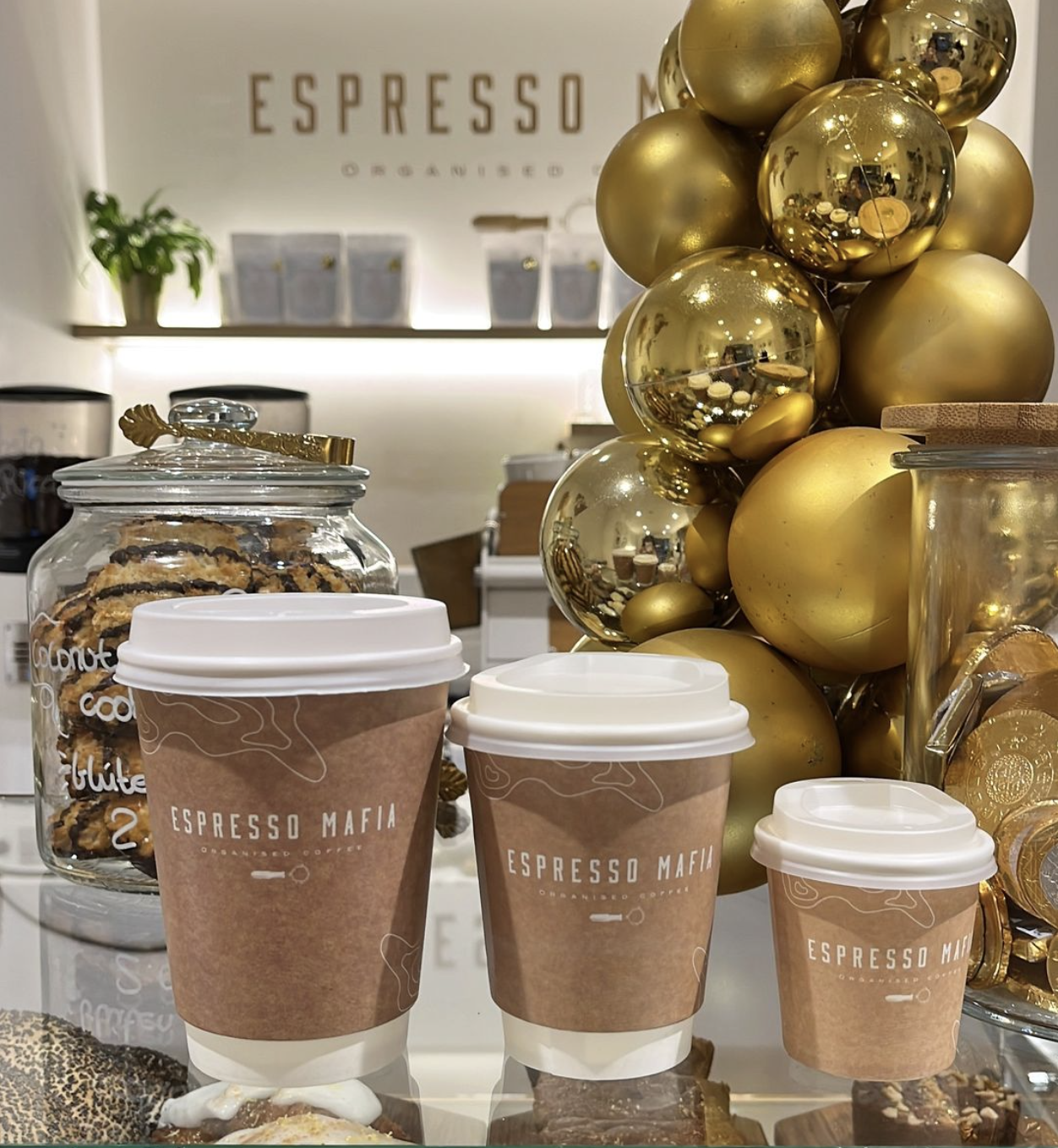 A display of brown branded coffee cups in three sizes arranged on a glass counter in a cozy café.