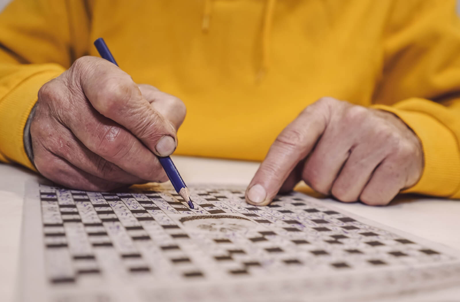 A close-up image of an older adult's hands with a pencil filling out a crossword puzzle.