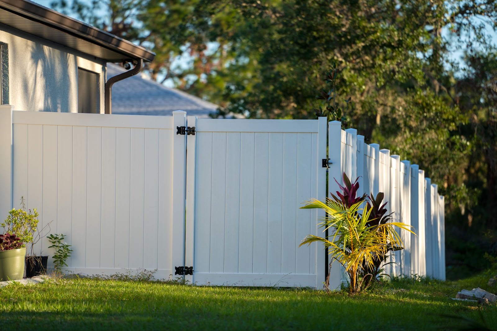 A close-up view of a white vinyl picket fence featuring a matching gate, set on a vibrant green lawn, enclosing a well-maintained property.