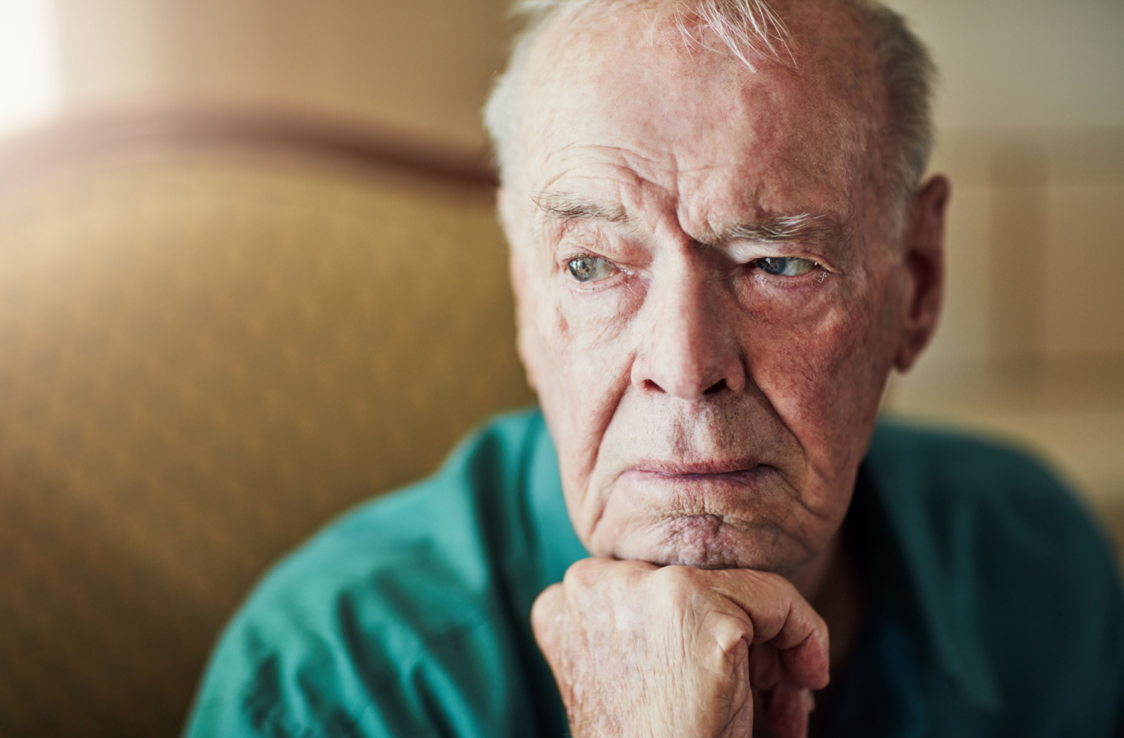 A senior with Alzheimer's sits calmly at home, looking longingly out the window.