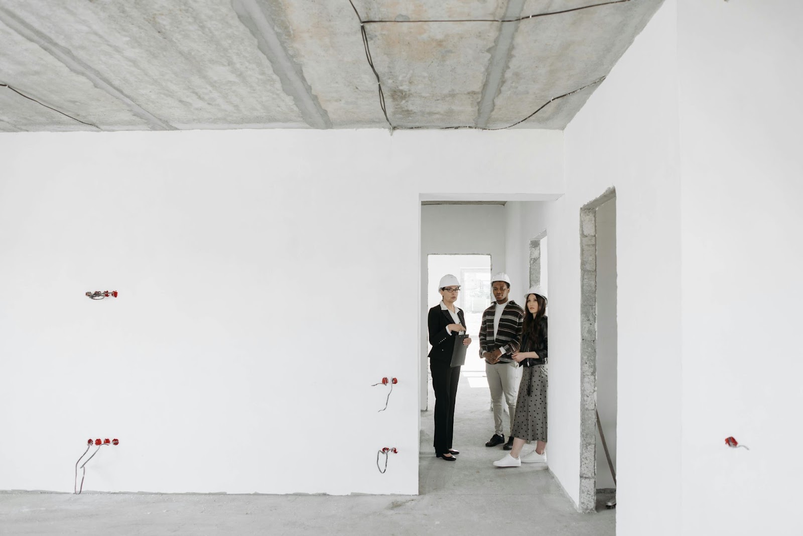 Three people wearing hard hats stand in an almost finished building project. 