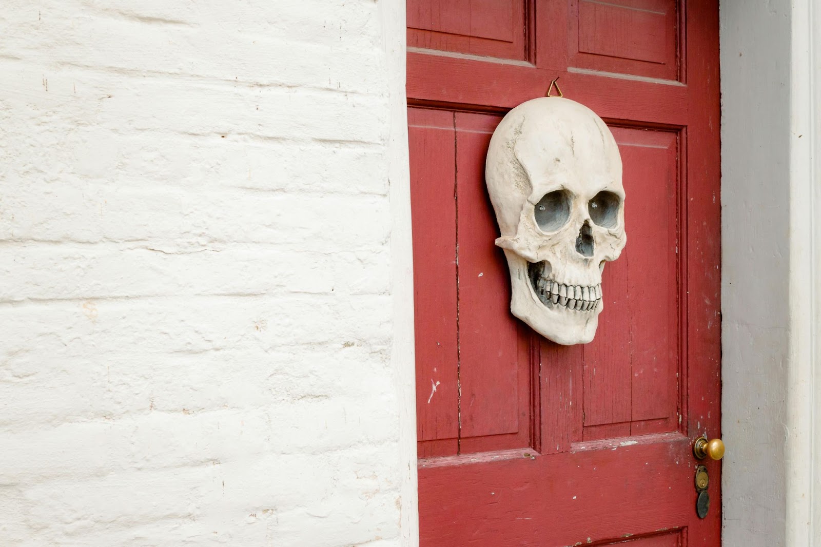 A red front door with a large decorative skull hanging as the door knocker