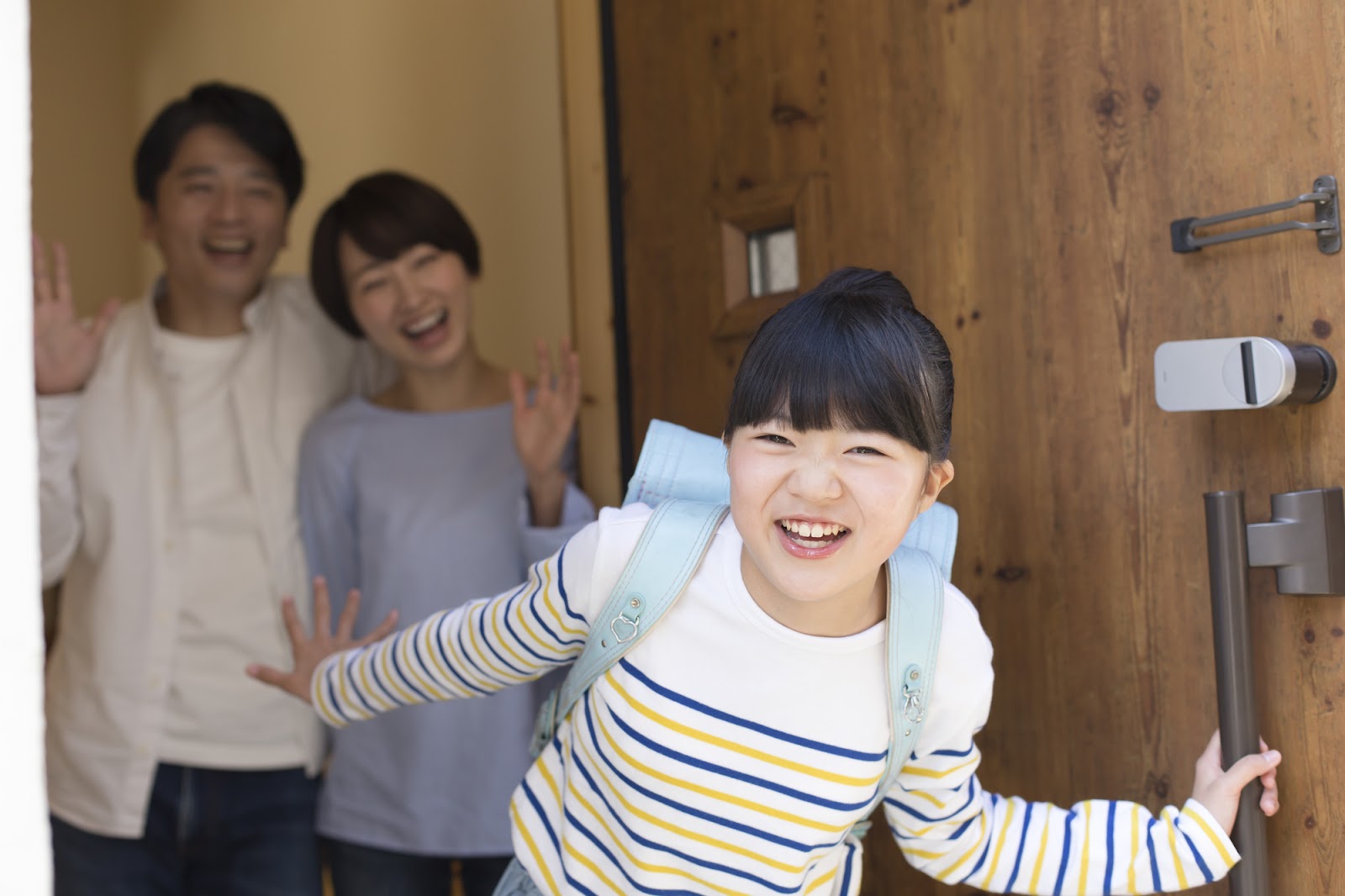 玄関で家族に見送られる笑顔の小学生