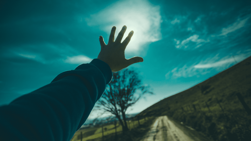 An outstretched hand reaching toward the sky on an open road, symbolizing ambition, growth, and the pursuit of personal development.
