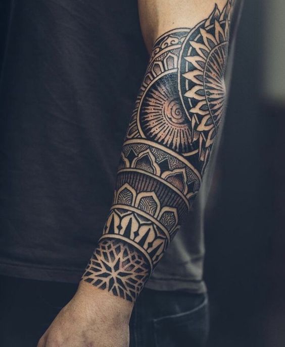 Intricate, geometric tattoo sleeve covering a person's forearm, featuring detailed and symmetrical patterns in black ink.