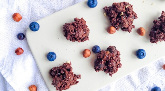 Chocolate clusters with blueberries and hazelnuts arranged on a white serving platter.