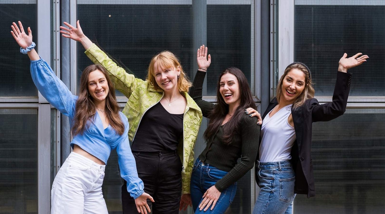 Four smiling registered dietitian standing together with raised arms, posing happily in front of a building.