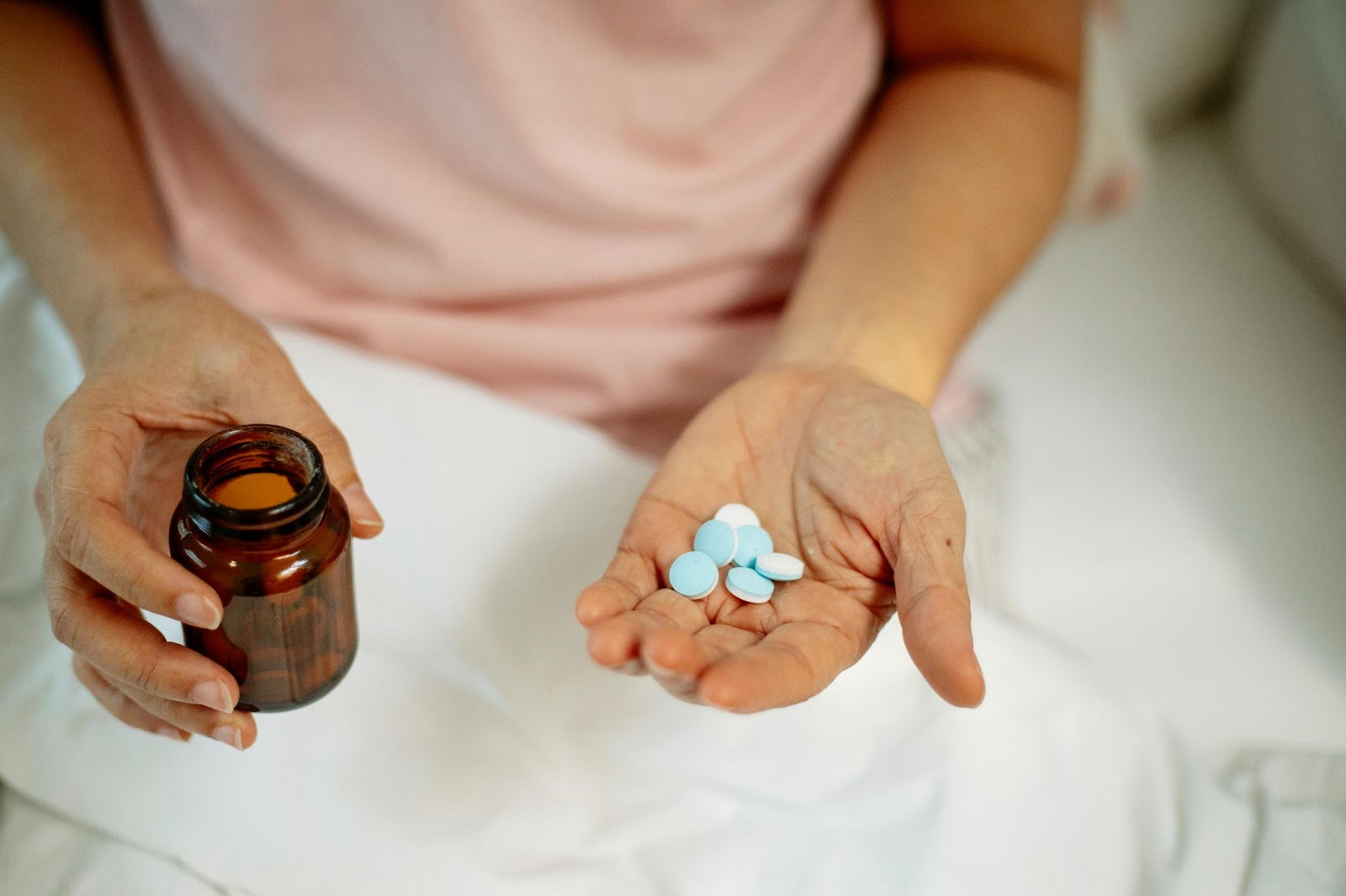 A person holding several pills in one hand and a pill bottle in the other hand