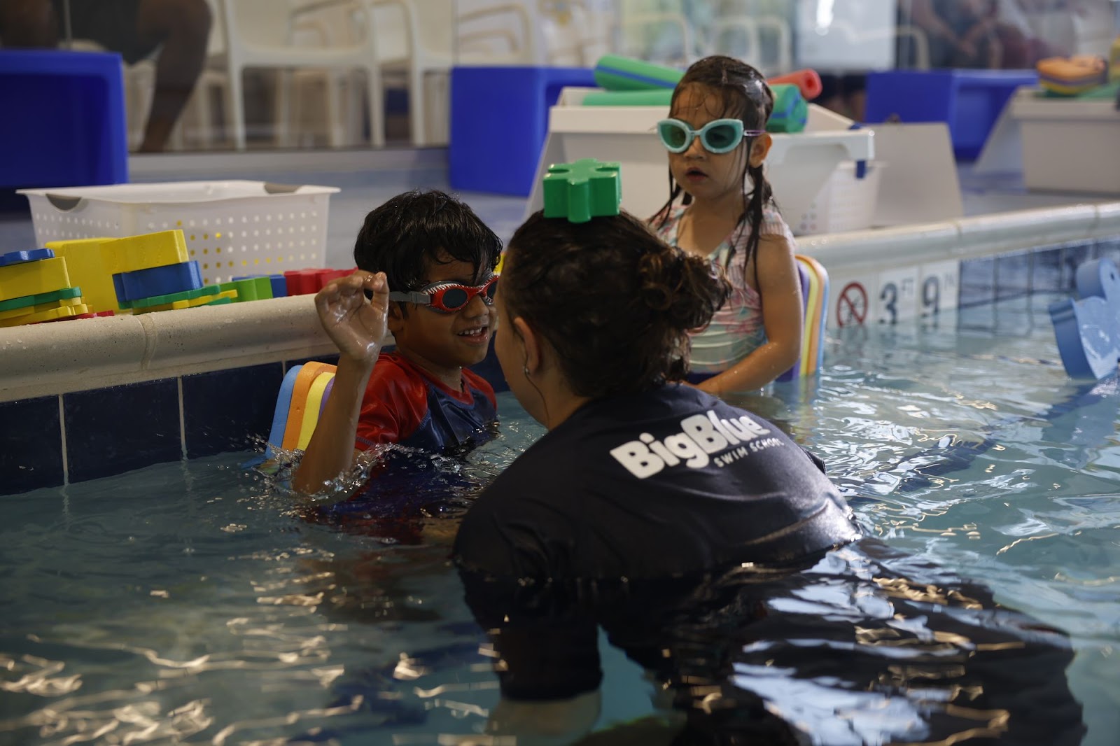 Swim instructor allowing a young boy to place swim toy on her head as he laughs