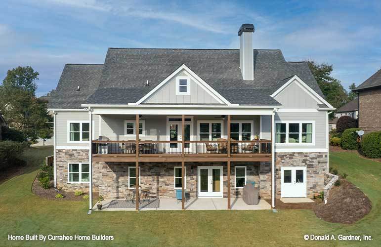 Rear exterior view with a covered porch and an upper balcony framed with wooden columns and wrought iron railings.
