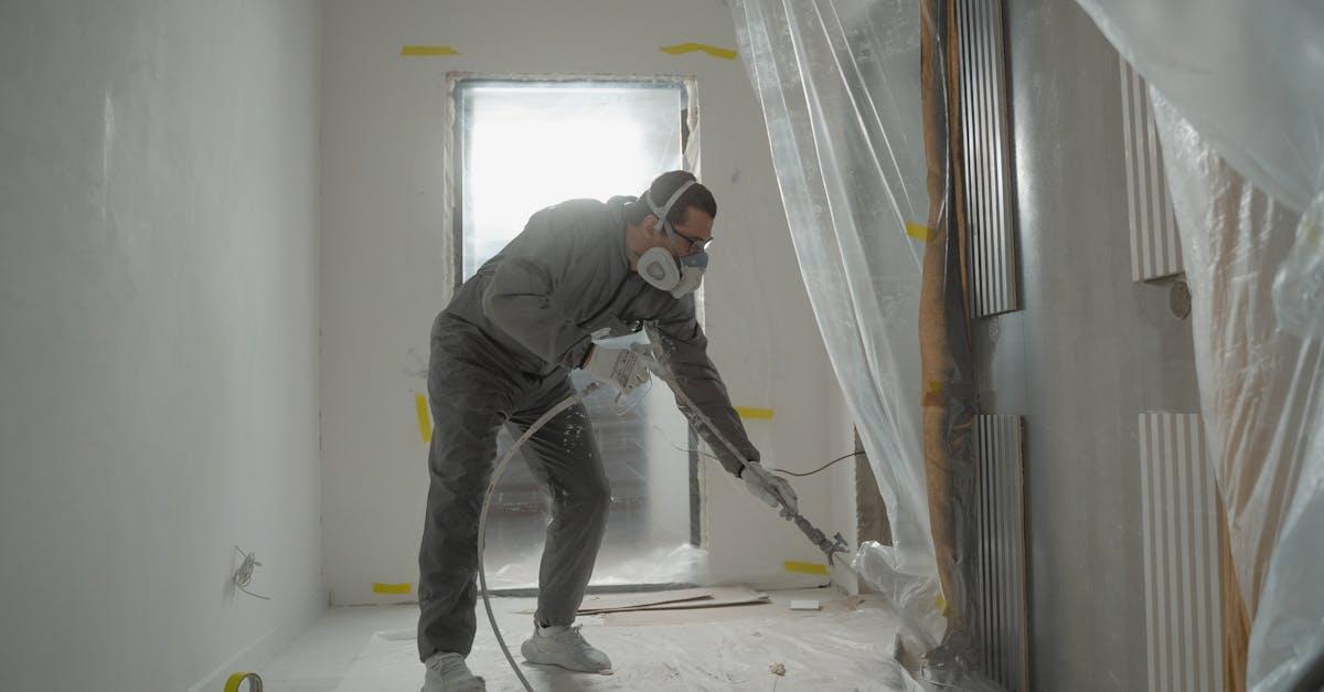 A worker in protective gear painting walls during an indoor renovation project.
