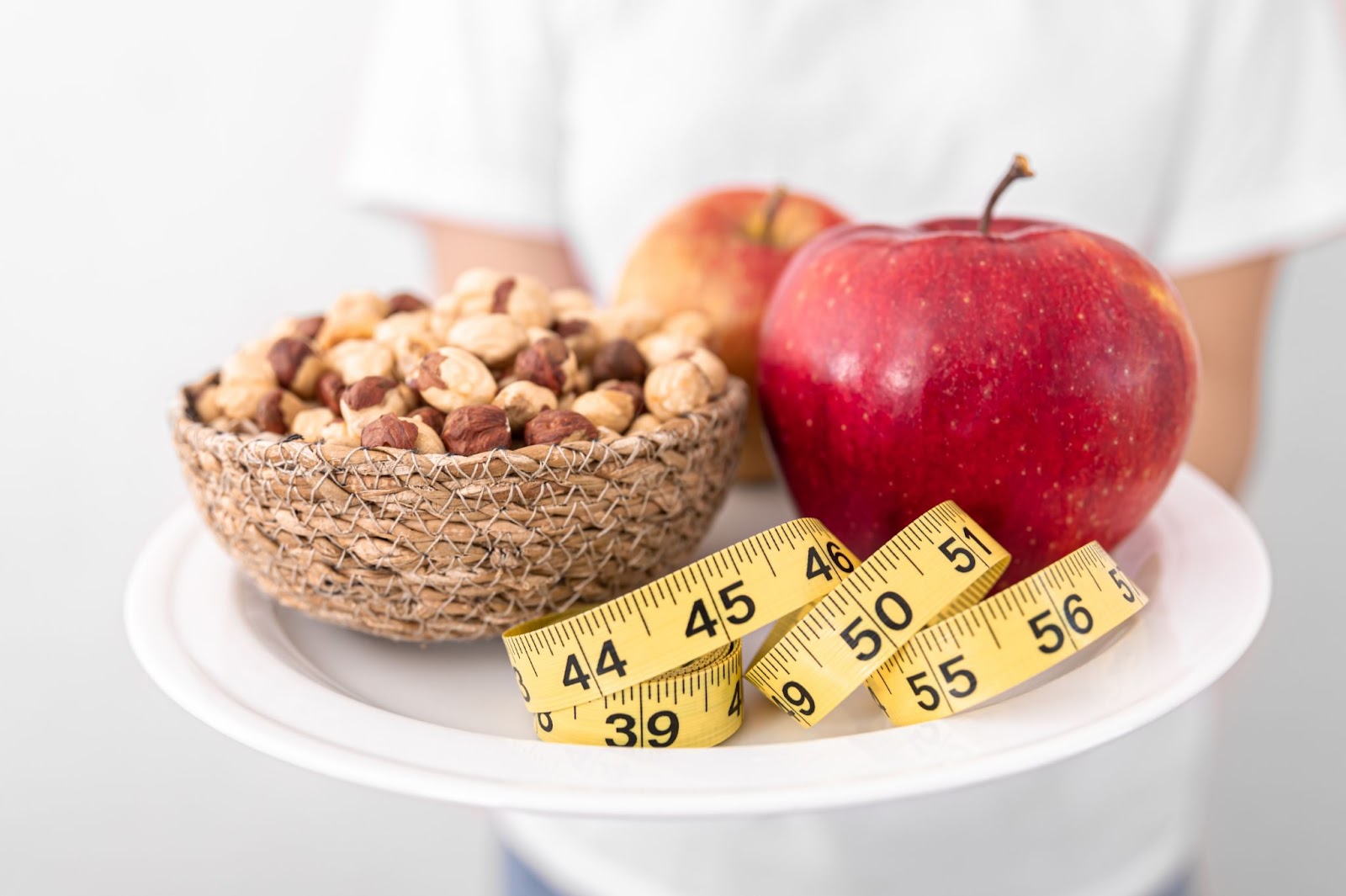 A picture of dry fruits and apples on a plate along with measuring tape.