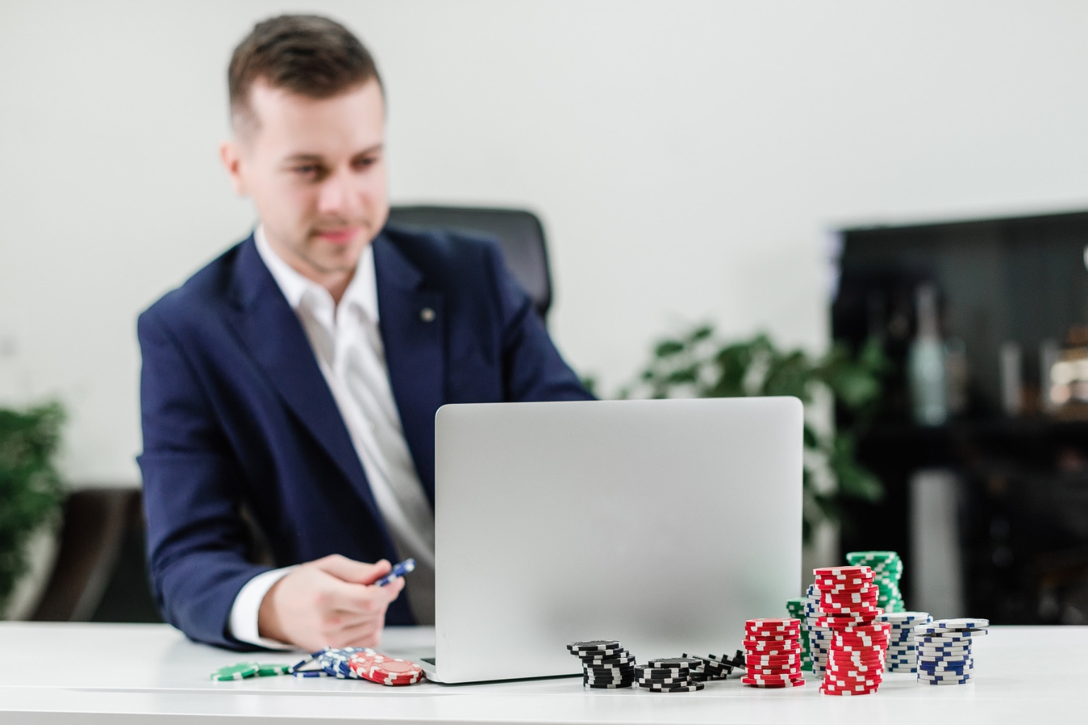 A man sits at a desk with a laptop and casino chips.