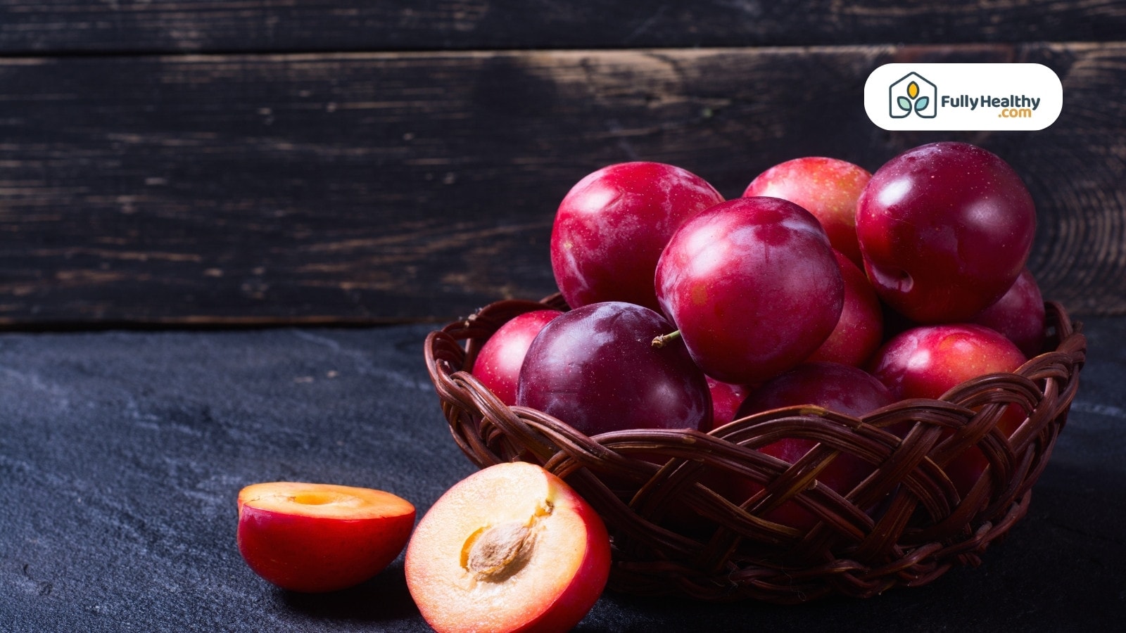Basket of ripe plums with sliced ones on dark surface