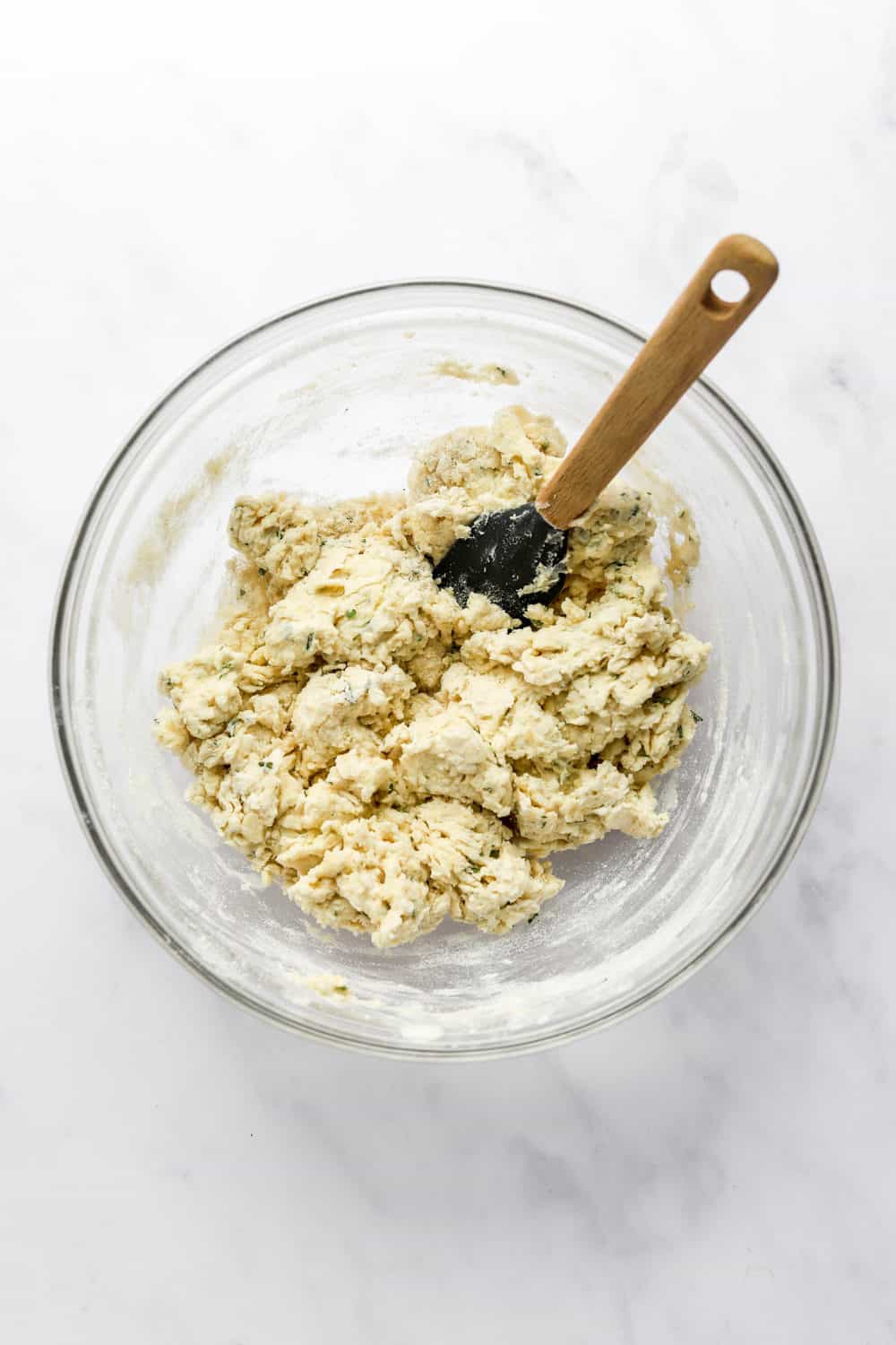 Naan bread dough in a glass bowl with a rubber spatula in the bowl.