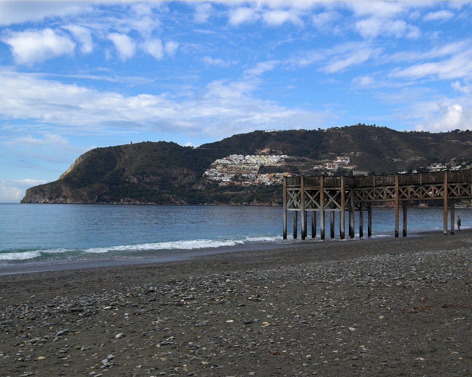 Beach with a dock and mountain in the background.