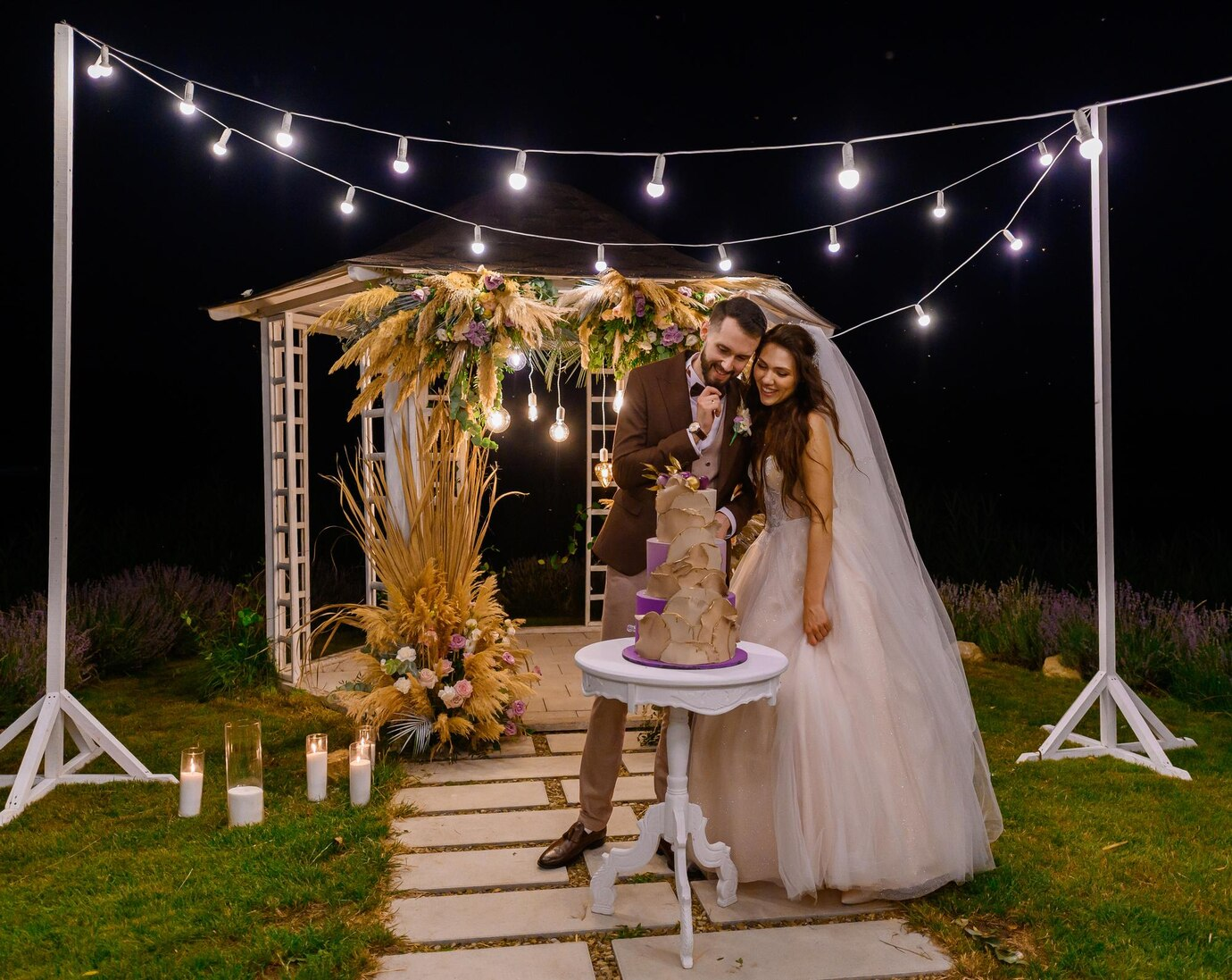 A beautifully decorated wedding gazebo set under a clear sky, adorned with flowing drapes, floral arrangements, and romantic lighting—perfect for an outdoor ceremony.