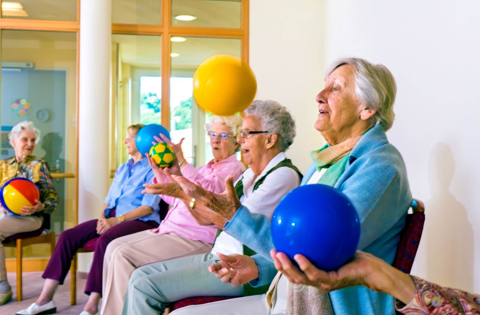 A group of seniors plays a ball toss game together with an assortment of colorful balls.