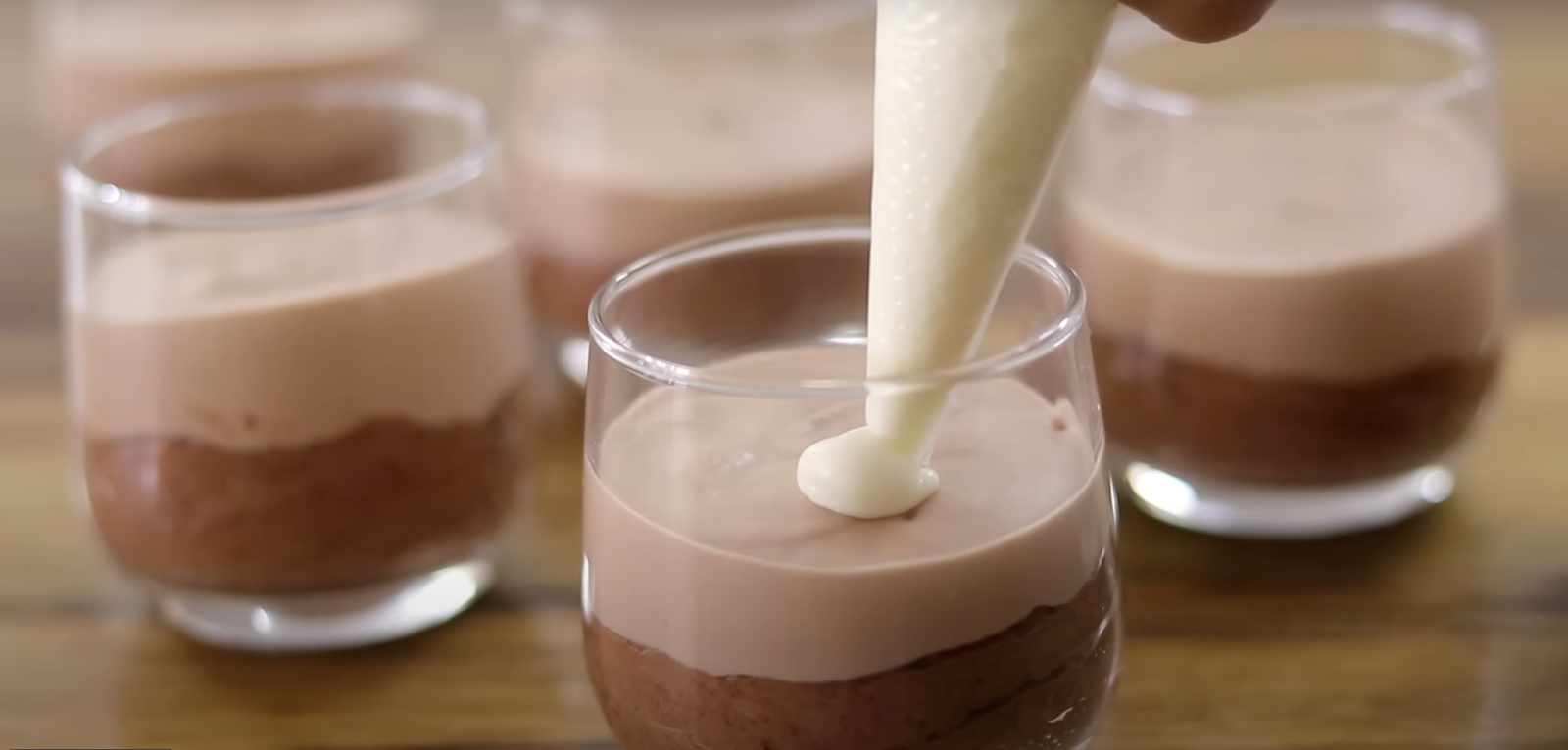 Pouring white chocolate mousse into a glass with sark chocolate mousse and milk chocolate mousse