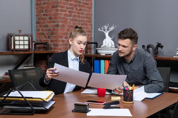 Top view of young busy and motivated clerical workers discussing one issue in the documents in the office