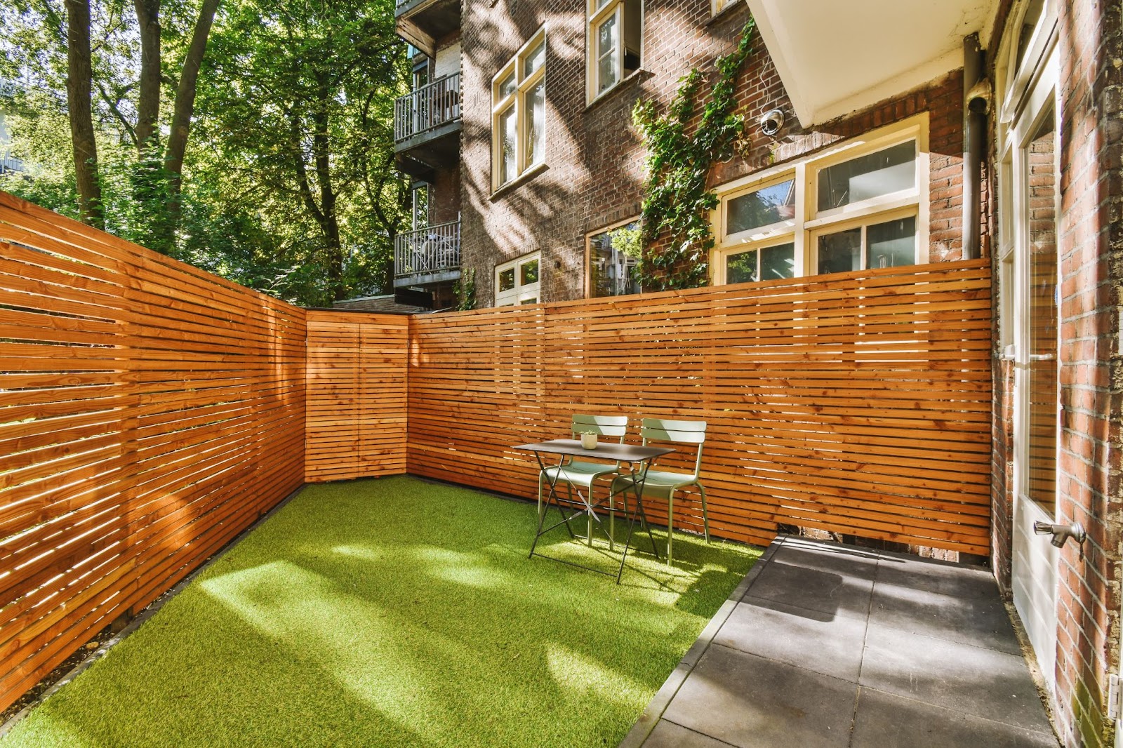 A small patio with Bermuda grass, bordered by a clean wooden fence, featuring two metal chairs and a table for a simple, cozy setup.