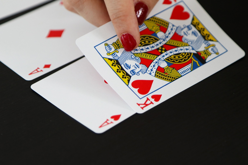 Close-up of a hand with red-painted nails flipping a king of hearts card on a black surface, with aces visible underneath.