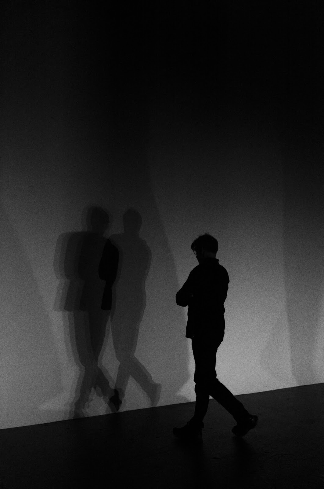 Photo of a silhouetted man contemplating shadows of himself on a wall.