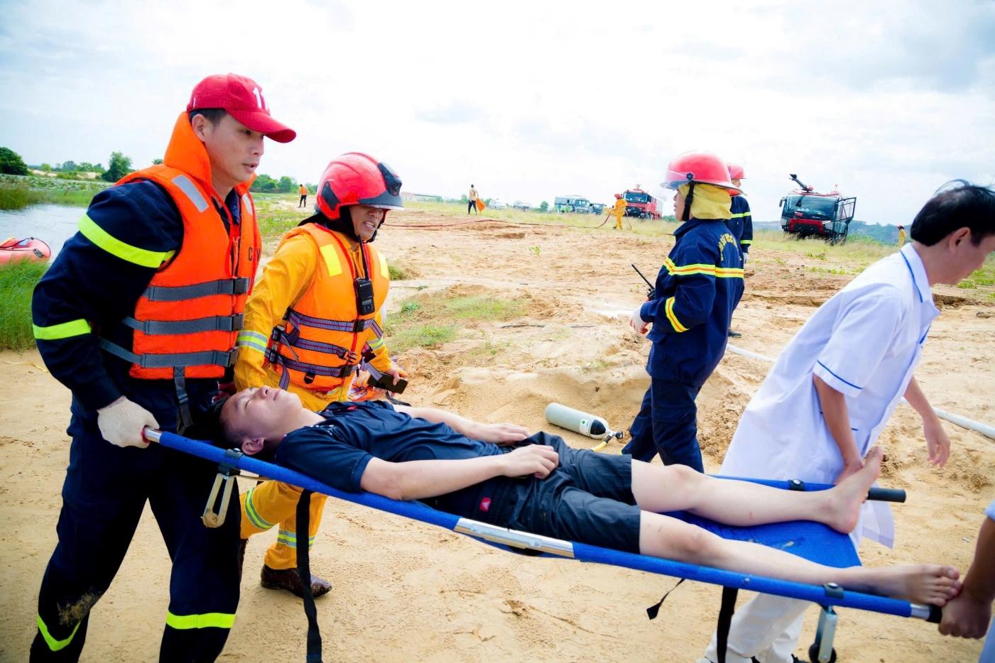 A group of people in orange vests and a person lying on a stretcherDescription automatically generated