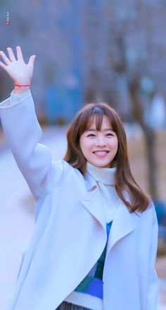 This contains an image of Park Bo Young wearing a white coat waves to the camera