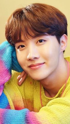 This contain BTS J-Hope is posing for a photo with his hand on his head and wearing a colorful sweater