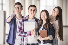 This contains an image of four young people smiling and posing for the camera with their notebooks in front of them