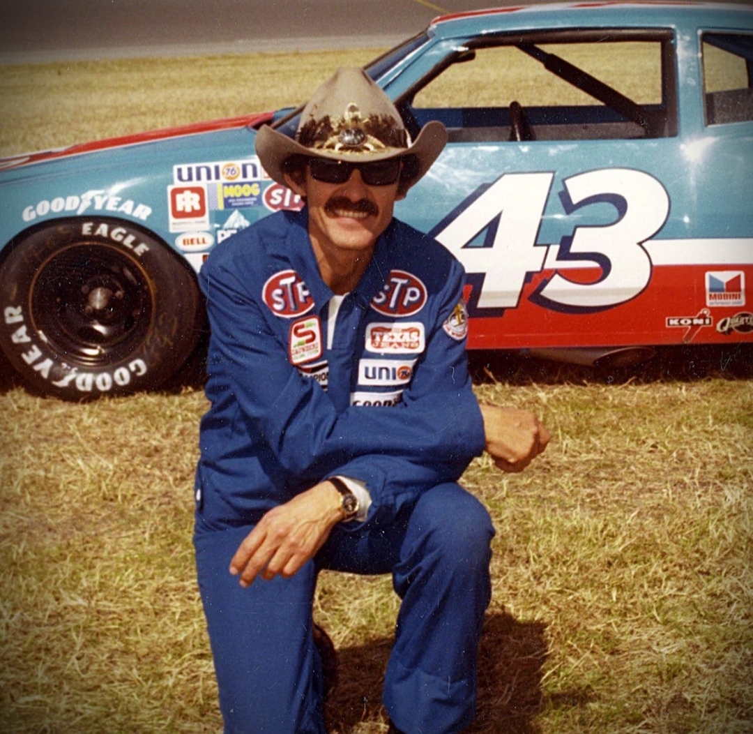 Richard "The King" Petty com seu carro da NASCAR número 43 ao fundo
