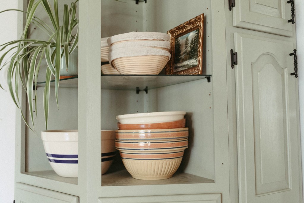 Stone bowls and banneton baskets sitting on a green shelf. 