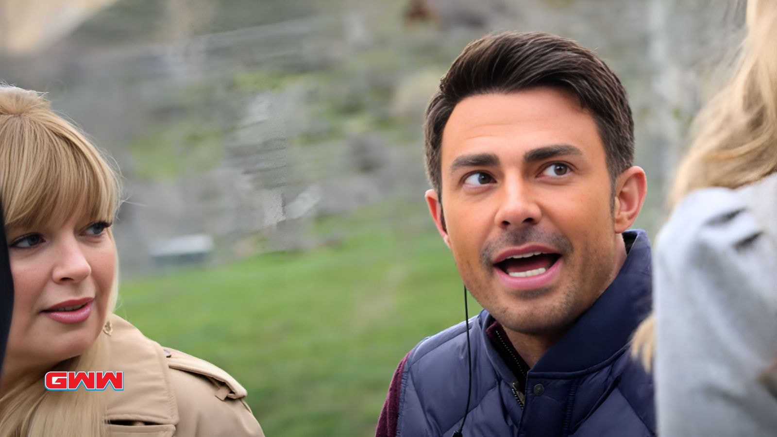 Jonathan Bennett in a blue jacket talks animatedly outdoors with two women.