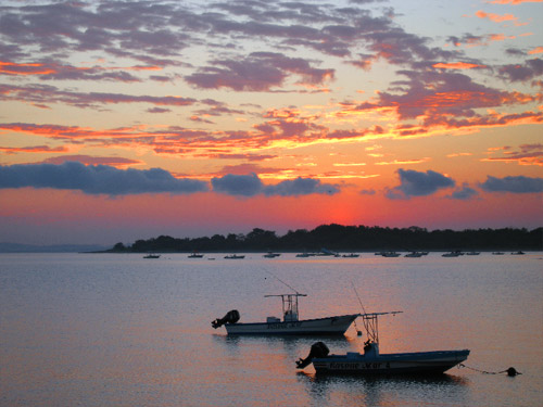 Boats are silhouetted by sunrise.