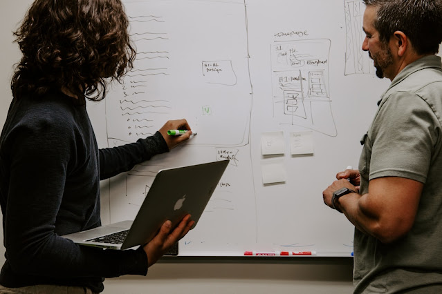 Two men standing in front of a whiteboard, engaged in discussion or presentation.