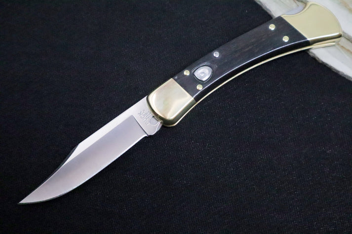 An image of the Buck 110 Folding Hunter Auto. It features a clip point 420HC stainless steel blade and an ebony wood handle with brass bolsters.