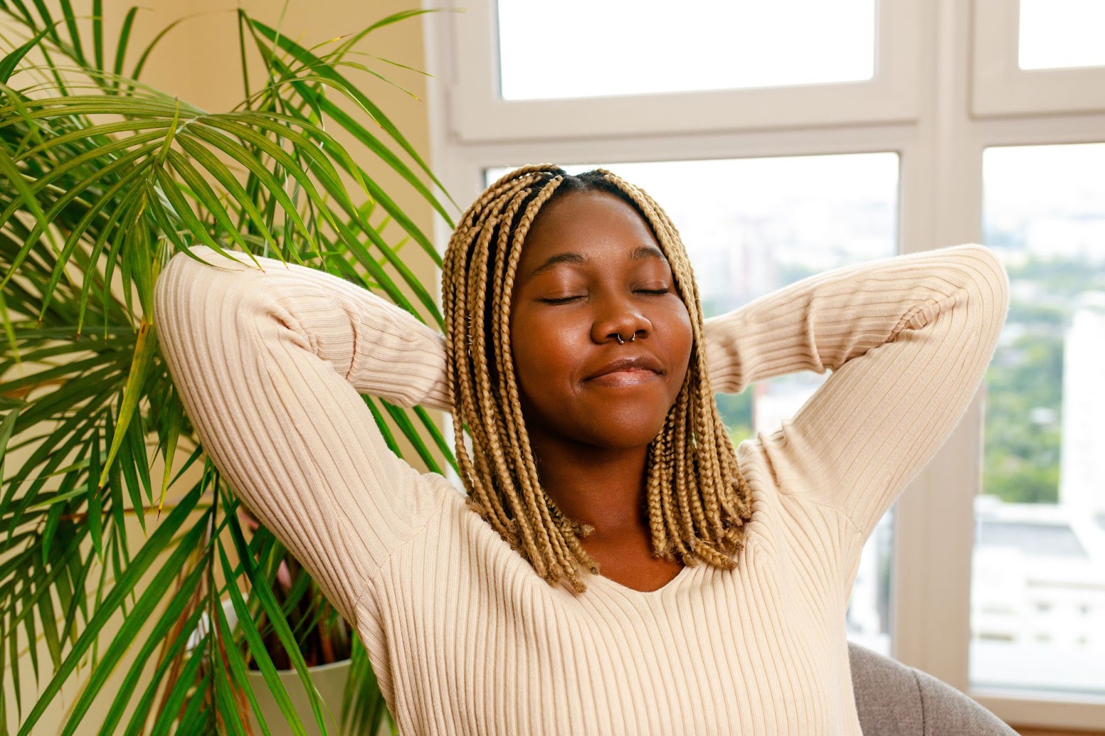 Relaxed woman with her hands behind her head and a plant in the background. 